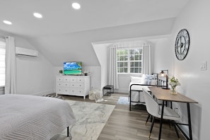 A modern bedroom with a bed, a desk, a chair, a TV, and a window with curtains.