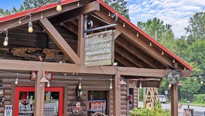 A rustic log cabin with a red roof, wooden signage, and string lights. - Private 1BR Retreat Among the Pines - Sleeps 4 - Unit 1 (Indian Trail)