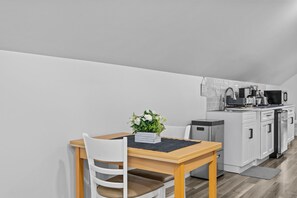 A modern kitchen with white cabinets, a wooden dining table, and a small potted plant.