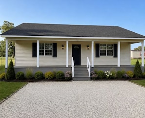 A single-story house with a front porch, a black front door, and a gravel driveway. - Cozy Cottage- 5min from Data Center! (Boyce)