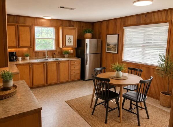 A kitchen with wooden cabinets, a stainless steel refrigerator, a dining table with chairs, and potted plants. - Cozy Cottage- 5min from Data Center! (Boyce)