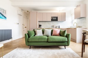 Ein modernes Wohnzimmer mit einem grünen Sofa, einem weißen Teppich und einer Küche im Hintergrund.