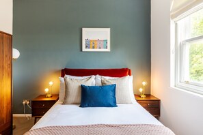 Ein Schlafzimmer mit einem Bett, zwei Nachttischen, einem Fenster und einem Wandbild.