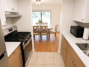 A modern kitchen with a gas stove, oven, microwave, and a sink. There is a dining area with a table and chairs. - New! CMU Getaway | Near Soaring Eagle & Campus (Mount Pleasant)
