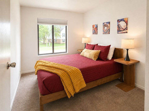 A bedroom with a bed, two bedside lamps, a window, and artwork on the wall.