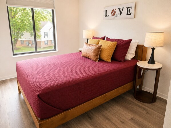 A bedroom with a large bed, two bedside lamps, a window with a view, and a wall sign that says 'LOVE'.