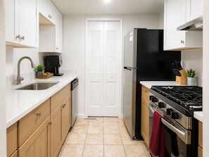 A compact kitchen with a stainless steel sink, a coffee machine, a black refrigerator, a stove, and wooden cabinets.