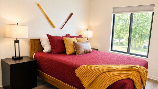 A bedroom with a bed, two nightstands, a window, and a view of greenery outside. - New! CMU Getaway | Near Campus & Soaring Eagle (Mount Pleasant)