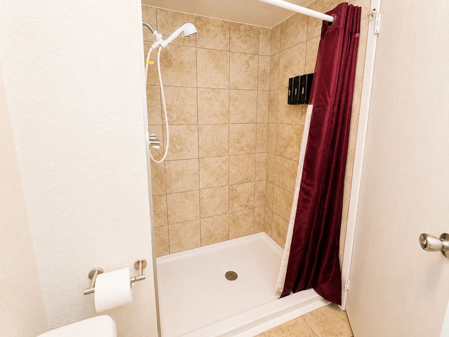 Un box de ducha con bañera blanca, cortina de ducha roja y paredes de azulejos beiges.