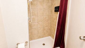 Un box de ducha con bañera blanca, cortina de ducha roja y paredes de azulejos beiges.