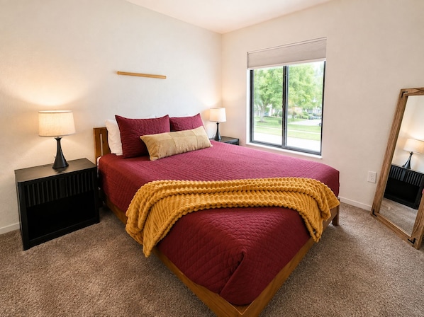 A bedroom with a large bed, two bedside tables, and a window with a view of greenery.