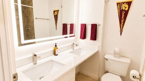 A bathroom with two sinks, a toilet, and a shower. There are towels hanging on a rack and a towel dispenser. - New! CMU Getaway | Near Campus & Soaring Eagle (Mount Pleasant)