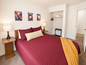 A bedroom with a large bed, two bedside tables with lamps, a wooden nightstand, a closet with a hanging rack, and three wall-mounted paintings. - New! CMU Getaway | Near Campus & Soaring Eagle (Mount Pleasant)