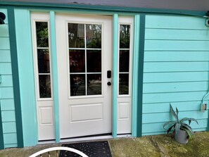 Une maison turquoise avec une porte d’entrée blanche, un petit porche et une plante en pot.
