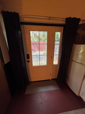 Ein Zimmer mit einer Schiebetür zu einer Terrasse und einem Sitzbereich, einem weißen Kühlschrank und einem kleinen Tisch mit Stühlen.