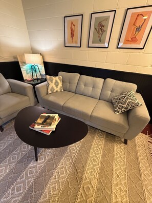 Un salon comprenant un canapé, un fauteuil, une table basse et des œuvres d’art encadrées accrochées au mur.