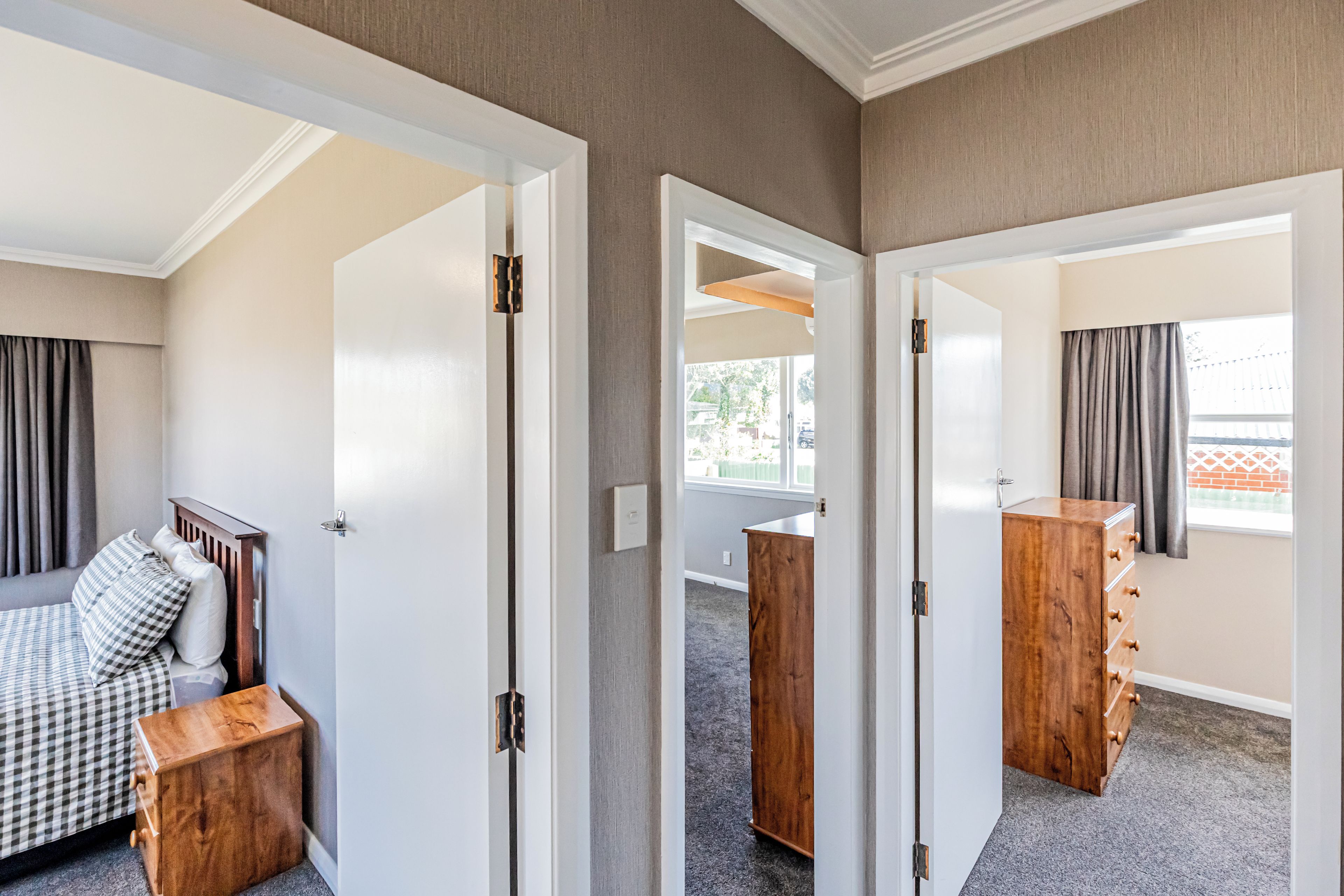A hotel room with a bed, a wooden nightstand, a wardrobe, and a window with curtains.