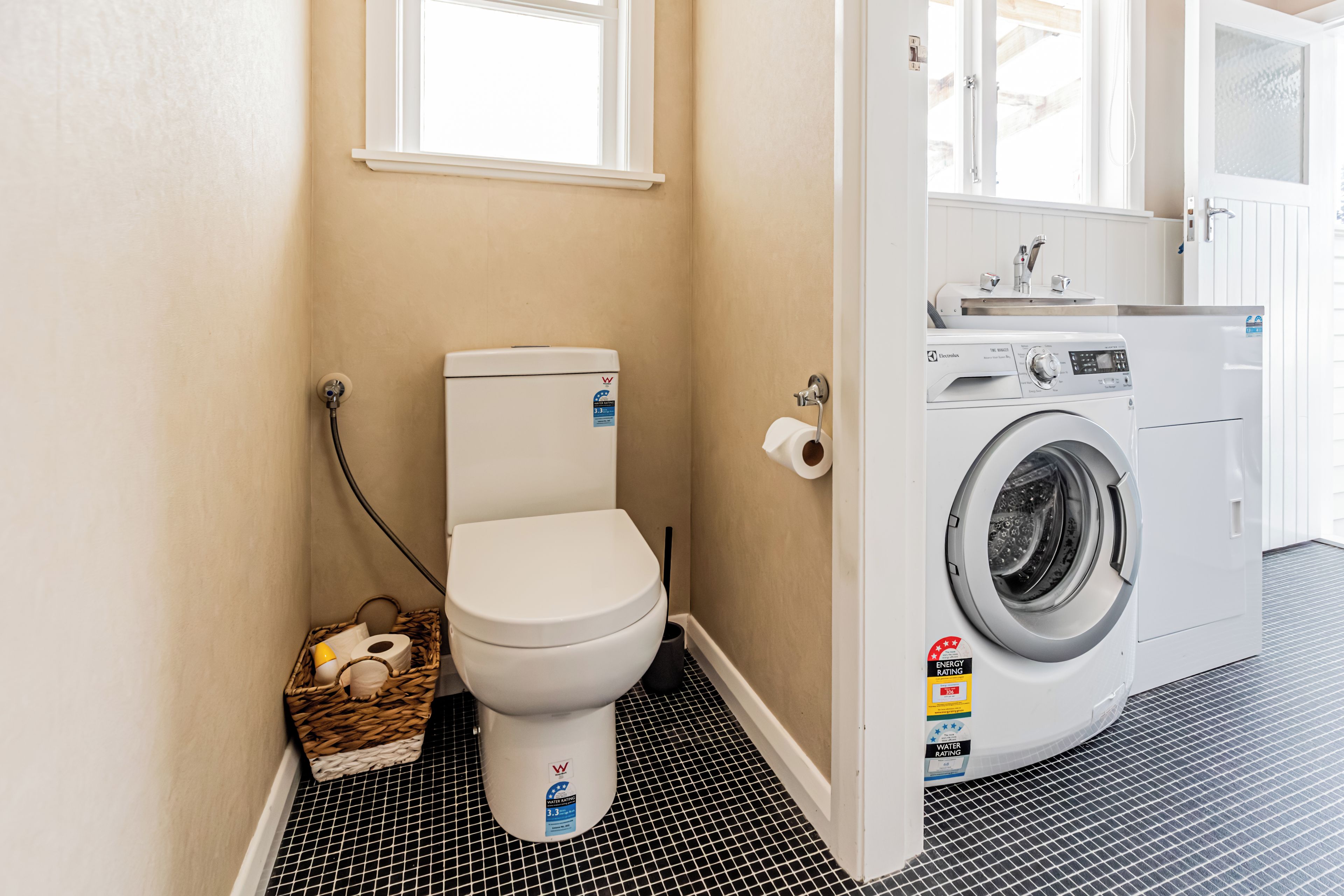 A compact bathroom with a toilet, a washing machine, and a small window.
