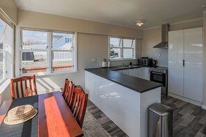 Una cocina moderna con una isla central, un comedor con mesa y sillas de madera, y grandes ventanales que ofrecen vistas al exterior.
