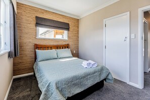 Un dormitorio con cabecera de madera, ventana con vistas, puerta y cama con colcha y toallas.