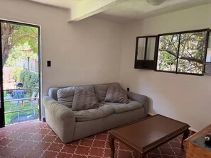 A room with a sofa, a wooden table, and a view through a glass door to an outdoor area with greenery. - Just 5 minutes from the archaeological site! Ideal family apartment with a garden (Malinalco)