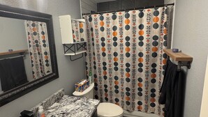 Un baño con lavamanos de mármol, inodoro, cortina de ducha con estampado de lunares y un perchero para toallas.