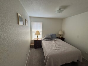 Ein Schlafzimmer mit einem Bett, zwei Nachttischen, einem Fenster mit Jalousien und einer Deckenleuchte.