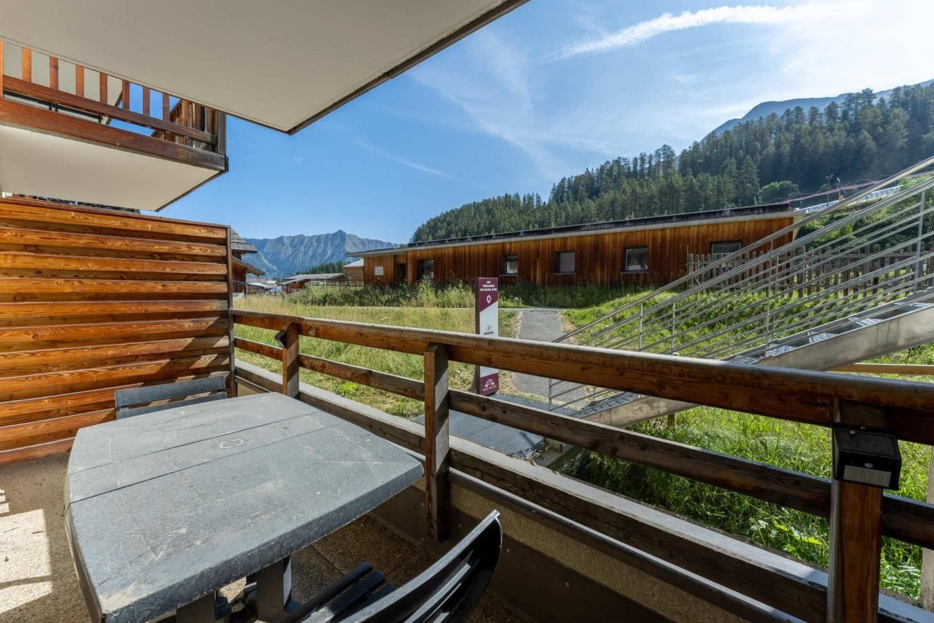 A wooden deck with a table and benches, overlooking a mountainous landscape with a building in the background.