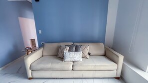 Un sofá color beige con almohadones, una mesita con una caja y una pared con detalles en azul.