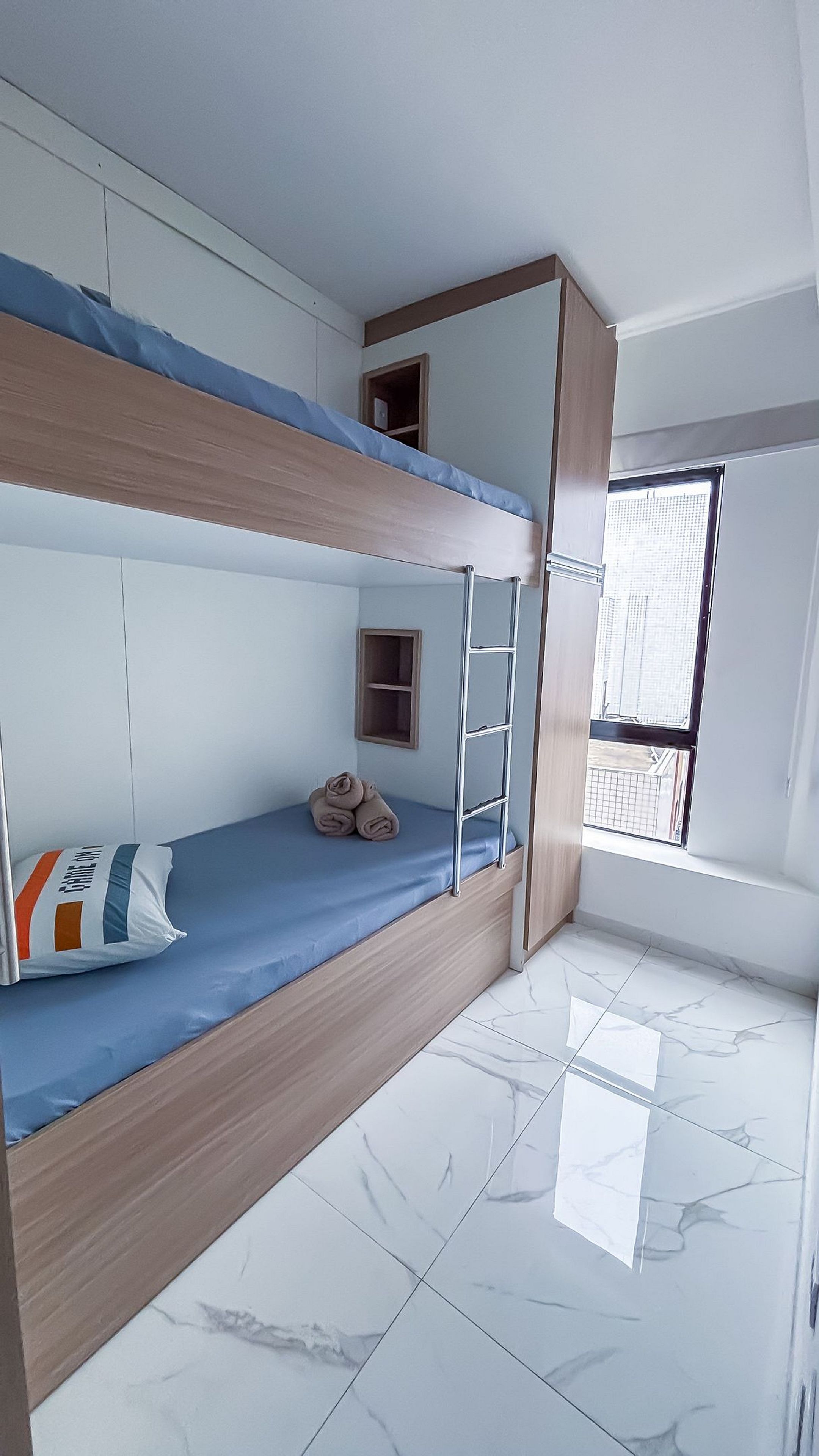 A bunk bed room with a window, a small shelf, and a tiled floor.