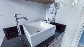 A bathroom with a white sink, a modern faucet, a hairdryer, and a towel dispenser.