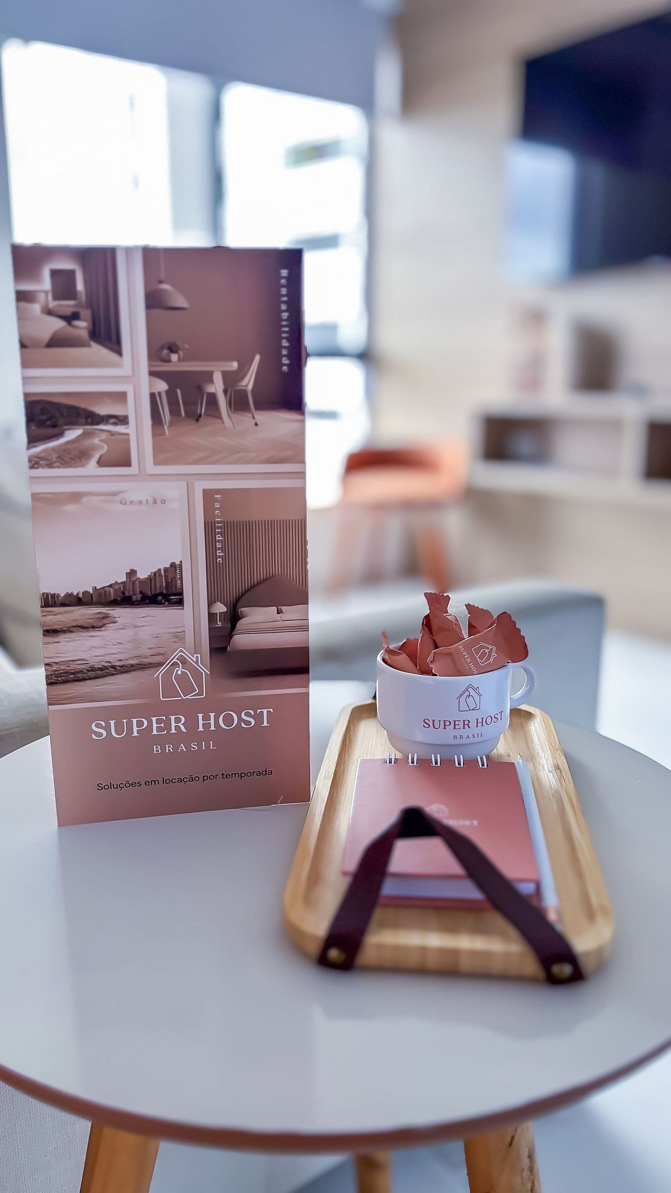 Un folleto titulado 'SUPERHOST BRASIL' con imágenes de un interior moderno, una taza de café y un cuaderno sobre una mesa.