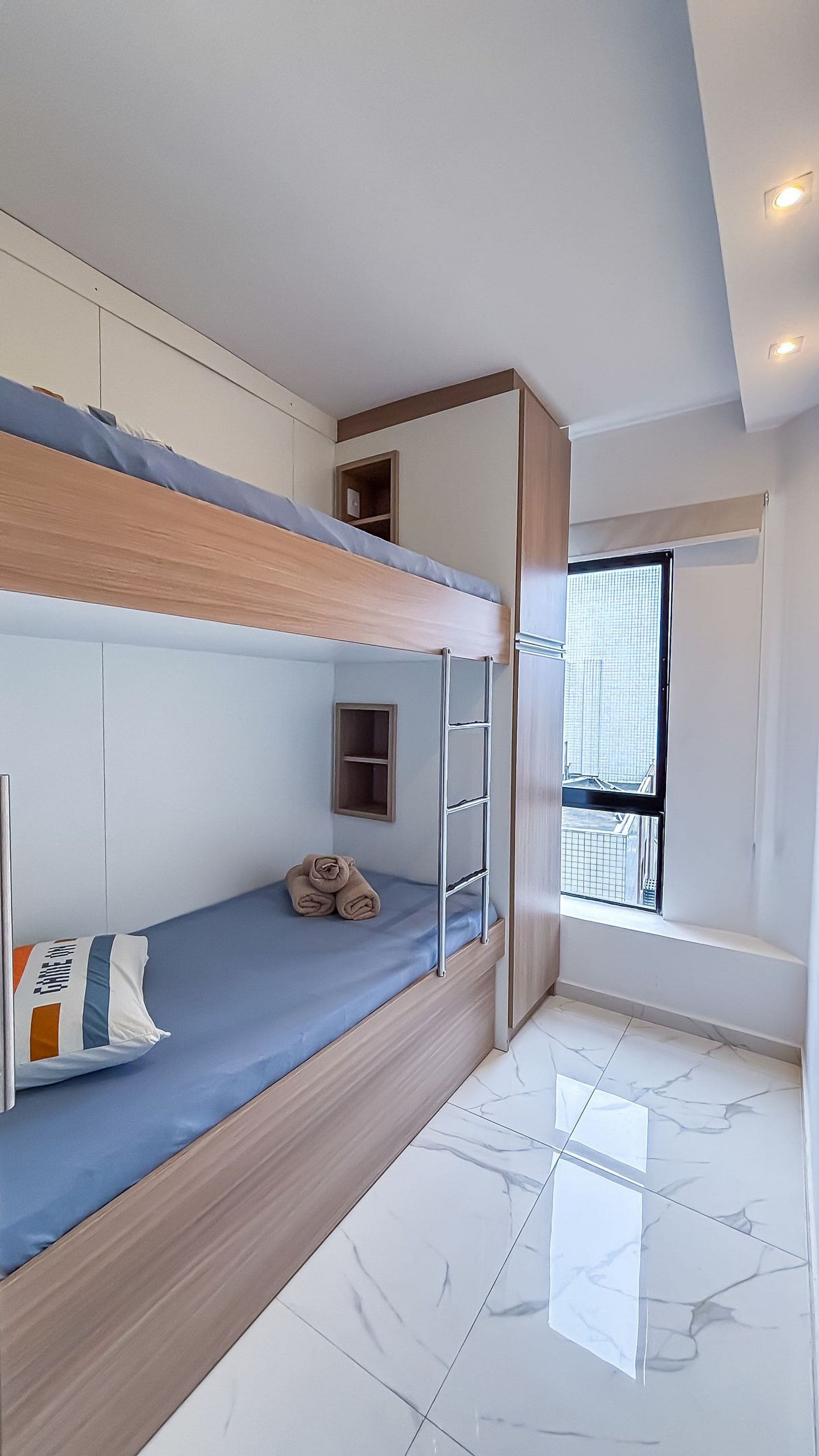 A modern bedroom with a bunk bed, a small shelf, and a window with a city view.