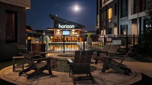 Un'area esterna con sedute, poltrone e un braciere, una piscina recintata e un edificio con un cartello che riporta la scritta 'horizon'.