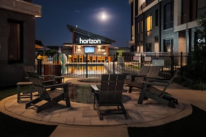 An outdoor seating area with chairs and a fire pit, a pool with a fence, and a building with a 'horizon' sign. - Brand New 4BR/4BA Home | Rooftop+Hot Tub+Sauna (Nashville)