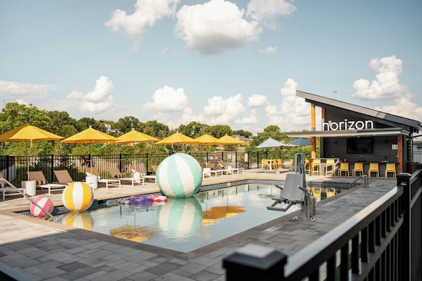 A pool area with lounge chairs and umbrellas, a large inflatable ball, and a building labeled 'Horizon.' - Brand New 4BR/4BA Home | Rooftop+Hot Tub+Sauna (Nashville)