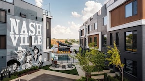 A modern building with a mural of Nashville, outdoor seating, and a pool area. - Brand New 4BR/4BA Home | Rooftop+Hot Tub+Sauna (Nashville)