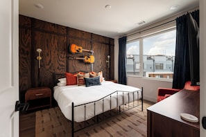 A bedroom with a bed, a guitar wall art, a window with curtains, and a view of buildings outside. - Brand New 4BR/4BA Home | Rooftop+Hot Tub+Sauna (Nashville)