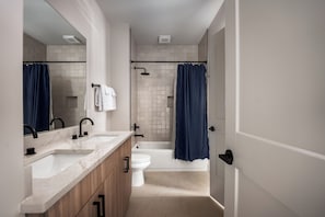 A modern bathroom with a double sink vanity, a bathtub, and a toilet. - Brand New 4BR/4BA Home | Rooftop+Hot Tub+Sauna (Nashville)