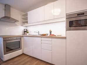 Cuina moderna amb armaris blancs, forn integrat, campana extractora d'acer inoxidable i taulell amb un solc i diversos objectes de cuina.