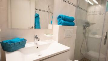A bathroom with a white sink, a mirror, a towel rack with blue towels, a shower with a glass door, and a toilet.