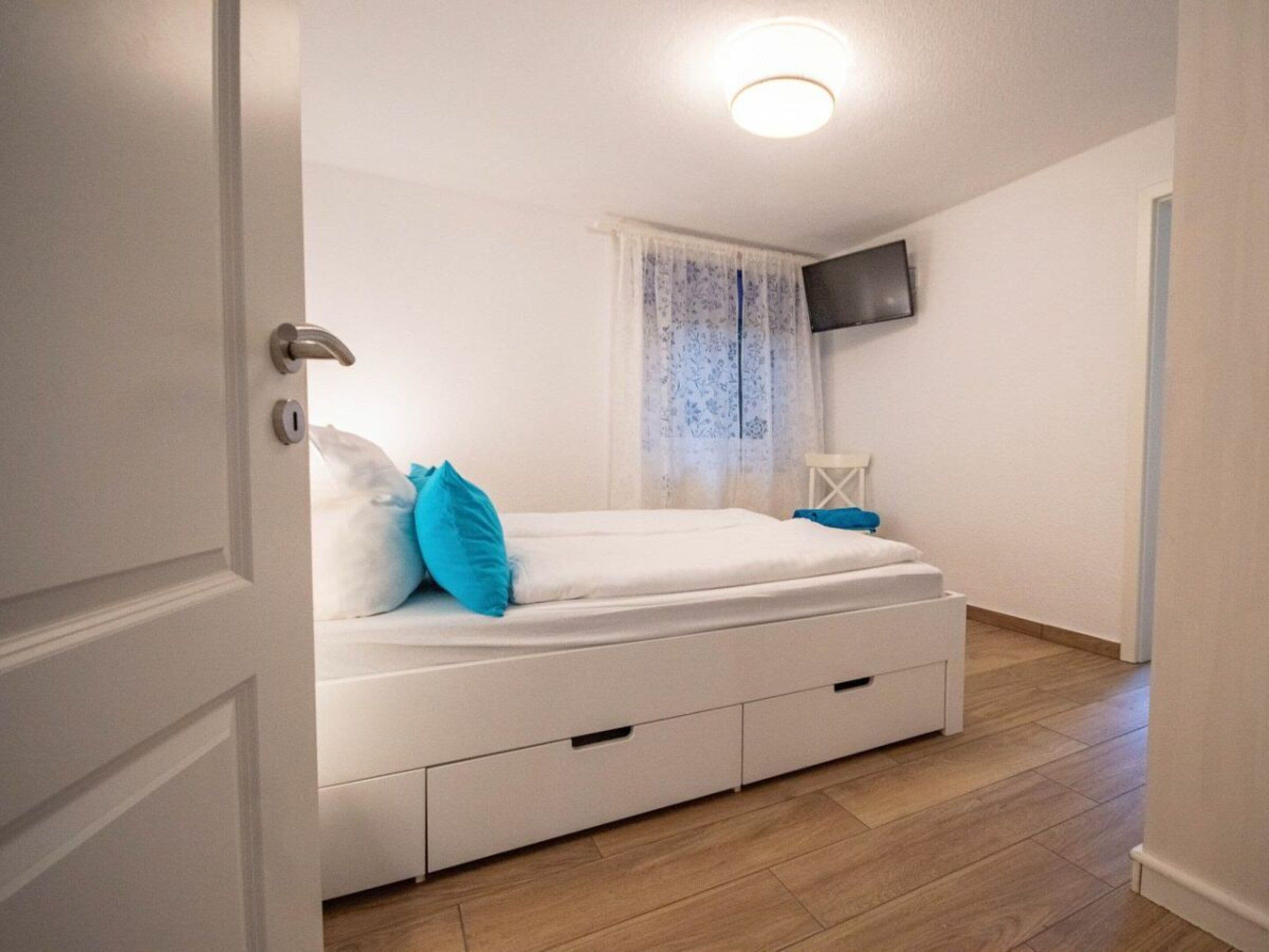 A bedroom with a bed, a television mounted on the wall, and a window with a curtain.