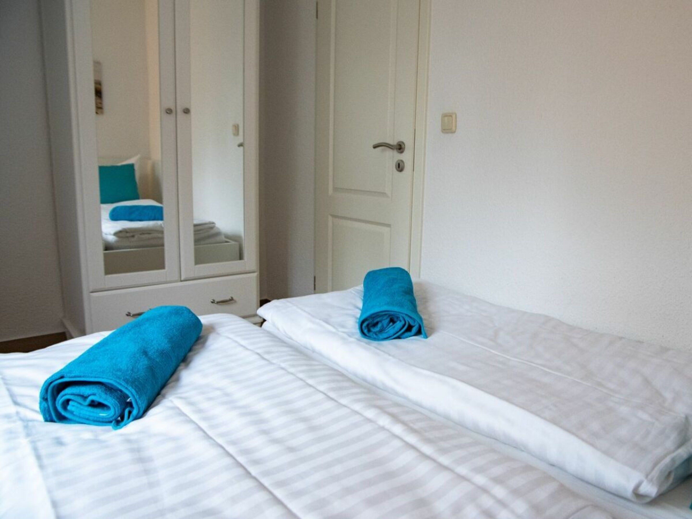 A hotel room with two beds, each with a rolled blue towel and white bedding.