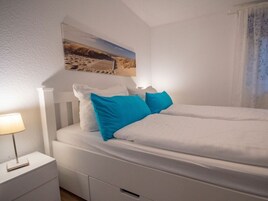 Un dormitorio con cama, mesita de noche, lámpara y un cuadro en la pared.