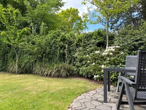 Un jardí amb un camí pavimentat, una taula i cadires.