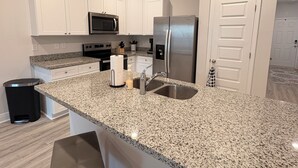 A modern kitchen with white cabinets, granite countertops, stainless steel appliances, and a large island with bar stools. - Fresh Townhome in Pensacola (Pensacola)