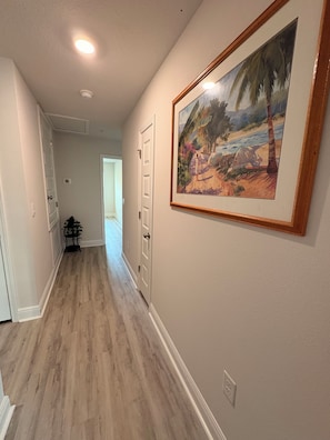 A hallway with wooden flooring, white walls, and a framed painting.