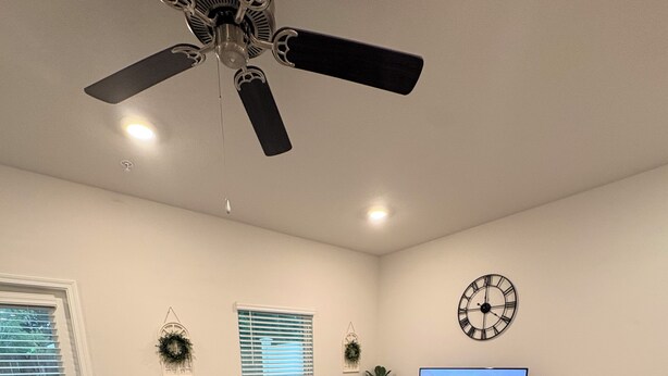 A modern living room with a sectional sofa, a flat-screen TV, a ceiling fan, and a decorative clock. - Fresh Townhome in Pensacola (Pensacola)