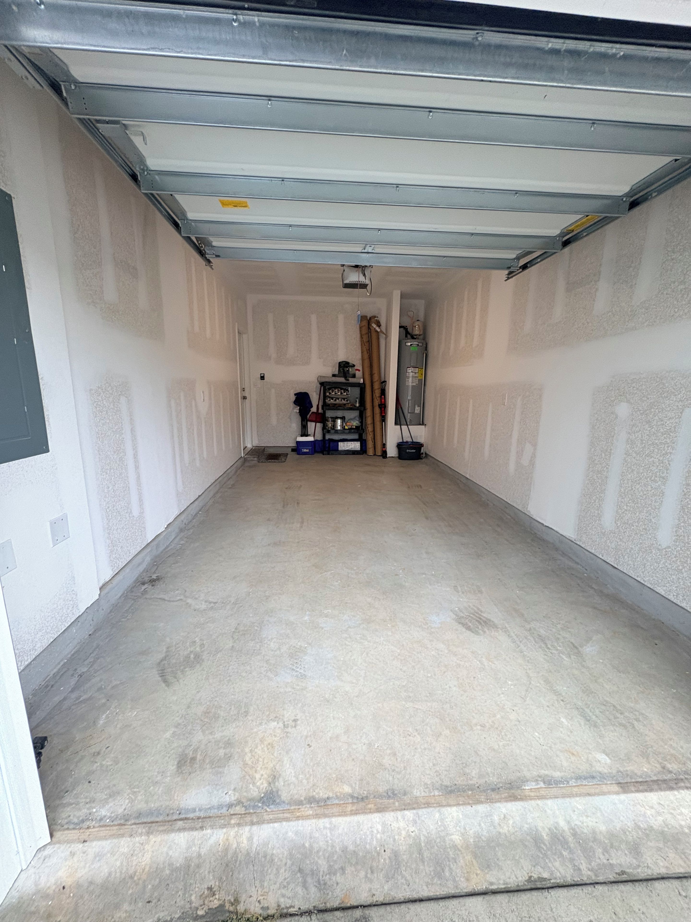 Uma garagem com piso de concreto, uma porta e uma prateleira com diversos objetos.