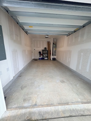 A garage with a concrete floor, a door, and a shelf with various items.